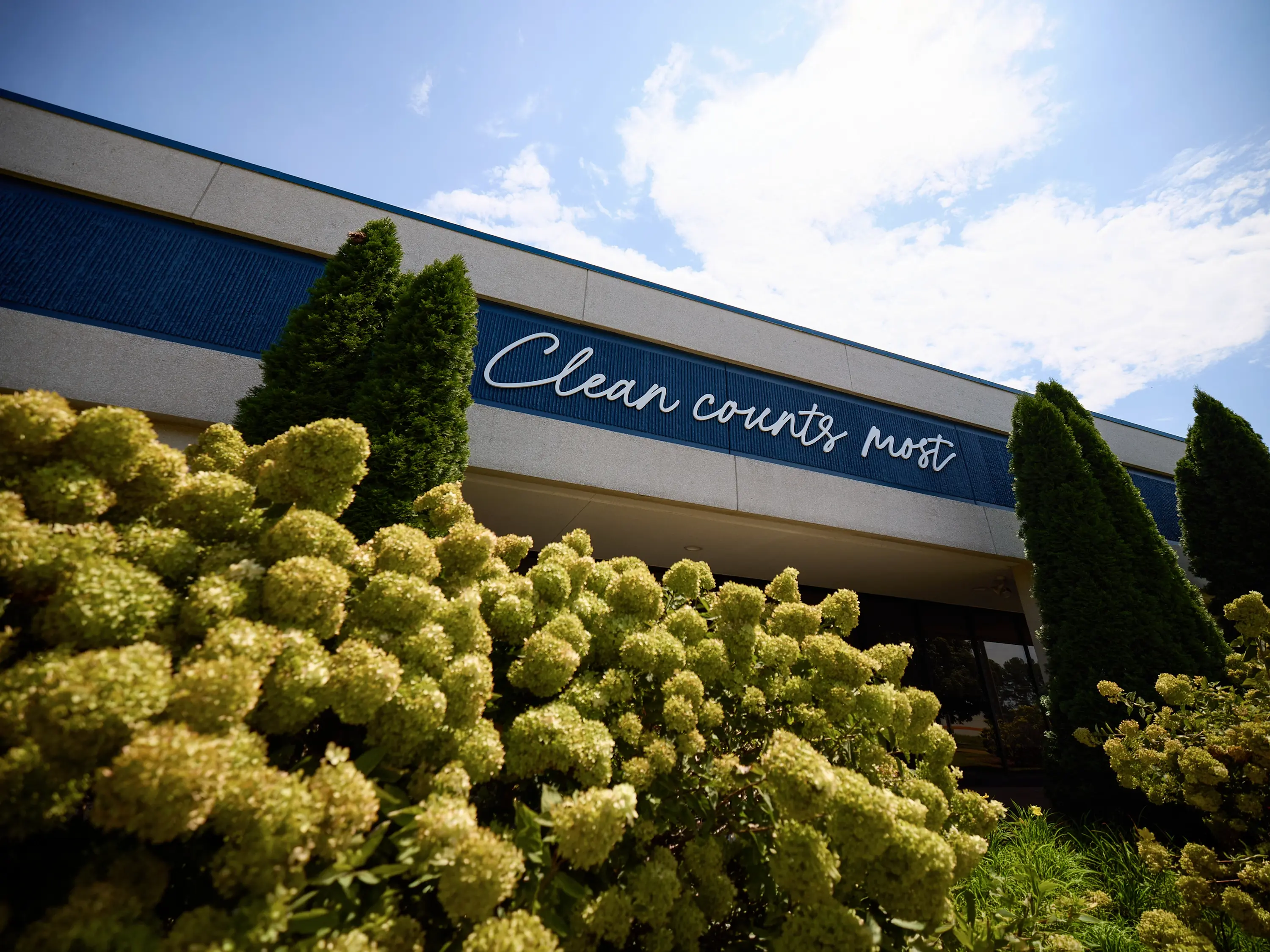 Exterior of a Contec facility with Clean counts most signage above landscaped flowering shrubs.